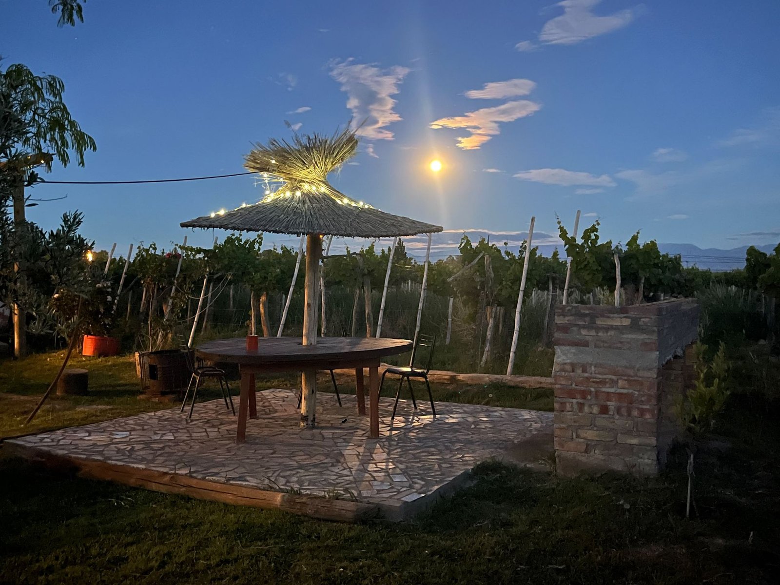 Quincho con techo de paja y mesa de madera iluminado bajo la luna llena en el complejo El Cordobés